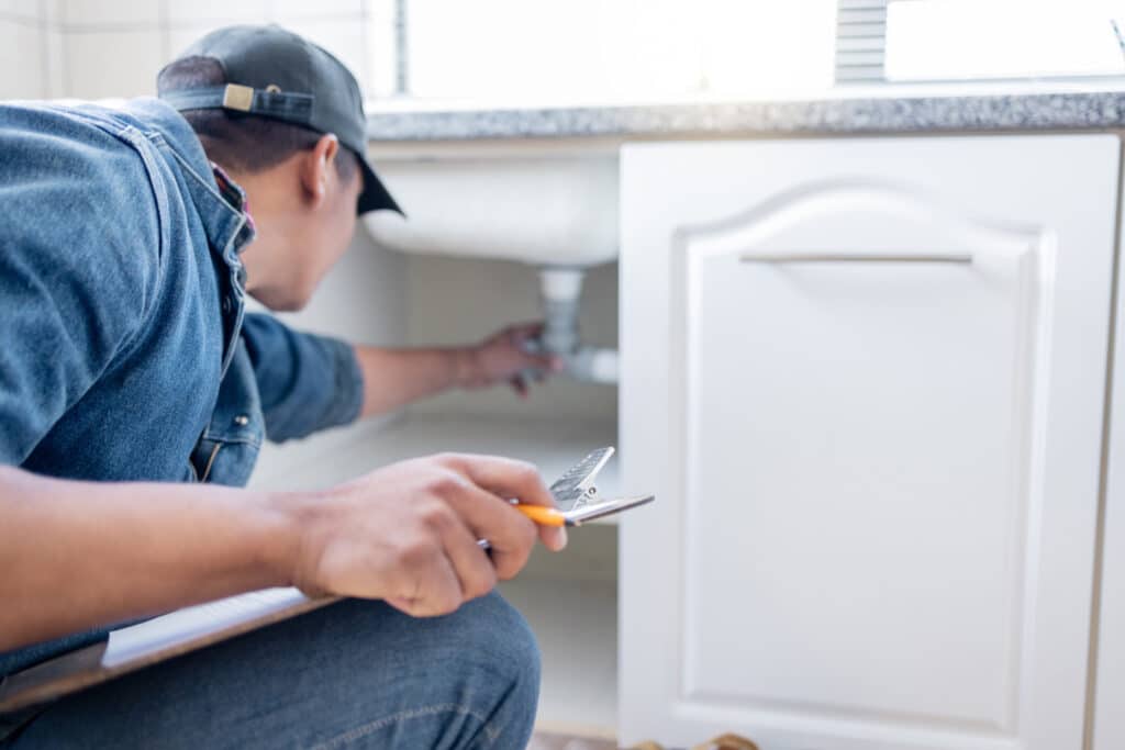 Professional plumber inspecting and adjusting under-sink plumbing during a residential service call by Burke Plumbing & Heating