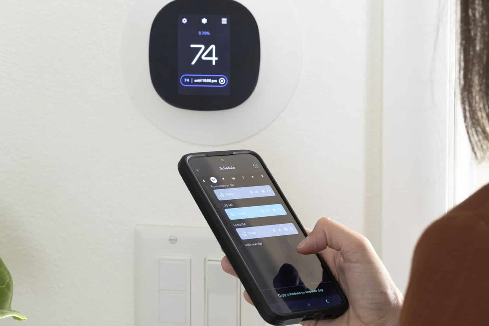 A woman using a smartphone to adjust the room temperature, Smart thermostat.